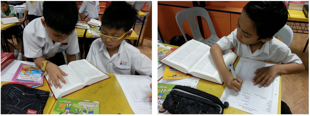 Two young students in white uniforms reading and writing at yellow school desks with open books.